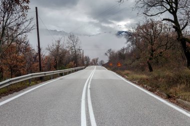 View of a forest and a rural road in the mountains on a cloudy, foggy, winter day (Greece, region of Thessaly)