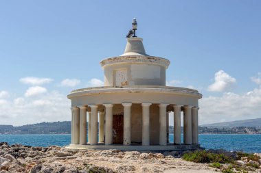 Eski, taştan, çalışan bir deniz feneri (Kefalonia Adası, Yunanistan) güneşli bir baharda denizin ve dağların arka planına karşı.