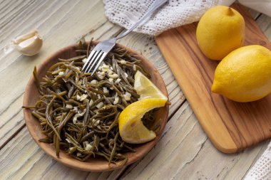 Salamura, deniz kenarı filizleri (Crithmum maritimum) aperatifi, ahşap bir masaya sarımsak ve limon yakın plan.