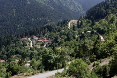 Güneşli bir yaz gününde dağların, köyün, ladin ormanlarının ve kırsal yolun manzarası (Güney Pindos Dağı, Yunanistan)