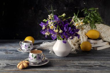 Kahvenin, tarla süsenlerinin, nergislerin ve limonların olduğu ahşap bir masa üzerinde sakin bir hayat.