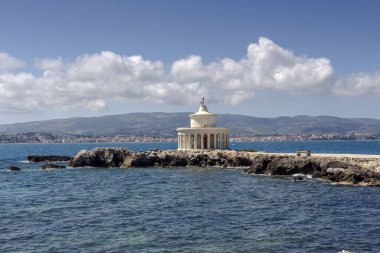 Eski, taştan, çalışan bir deniz feneri (Kefalonia Adası, Yunanistan) güneşli bir baharda denizin ve dağların arka planına karşı.