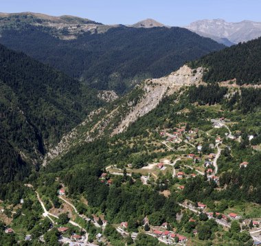 Güneşli bir yaz gününde dağların, köyün, ladin ormanlarının ve kırsal yolun manzarası (Güney Pindos Dağı, Yunanistan)