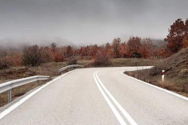 Kışın dağlarda (Yunanistan 'ın Epirus bölgesi) bulutlu ve sisli bir günde kırsal ve ıssız bir yol manzarası