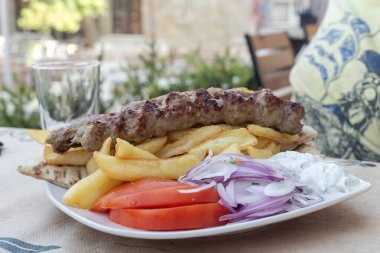 Ünlü, geleneksel Yunan atıştırmalıkları (kebap) bir sokak büfesinde yakın plan beyaz bir tabakta yatıyor.