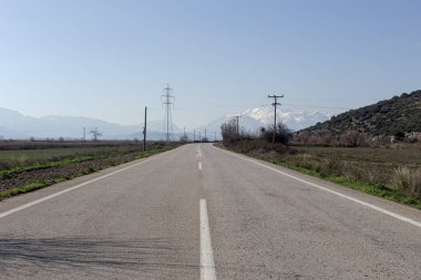 Güneşli bir kış gününde dağların ve tarlaların manzaralı kırsal yol (Yunanistan)