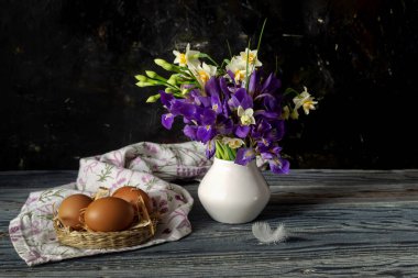 Paskalya kompozisyonu. Narsisli ve irisli bir buket, ahşap masa üzerinde eski usul yuva ve yumurtalar.