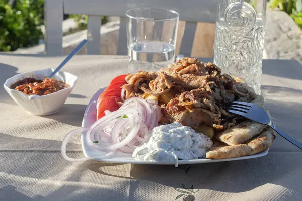 Yunan yemeği. Geleneksel Yunan kızarmış domuz parçaları (gyros) soslu, sebzeli ve bir meyhanedeki masada patates kızartması.