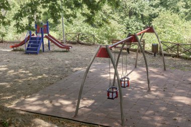 Güneşli bir yaz gününde, bir şehir parkında salıncaklar ve dinlenme alanları olan küçük bir kasabada (Yunanistan 'ın orta kesiminde) modern oyun parkı