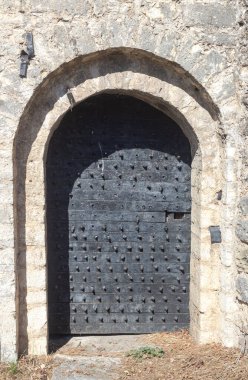 Doku, desen. Arka plandaki eski bej duvar, siyah demir retro kapılı doğal taştan yapılmış.