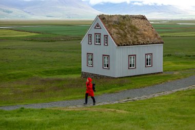 A girl in a red jacket runs near a peat-roofed house in Iceland. Glaumbaer