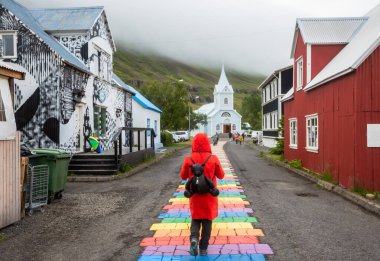 Kırmızı ceketli turist Seydisfjrur, İzlanda, İskandinavya, Avrupa 'da Gökkuşağı Yolu boyunca yürüyor