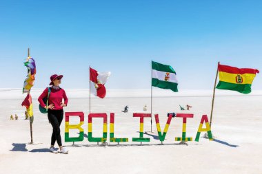 Bayrakların yanında duran şapkalı bir kız. Salar de Uyuni. Bolivya