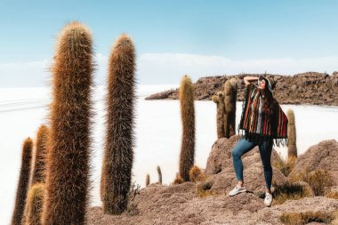 Pançolu ve şapkalı bir kız büyük kaktüslerin arasında bir taşın üzerinde duruyor. Incauasi Adası, Salar de Uyuni. Bolivya