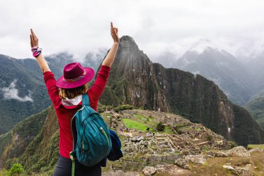 Machu Picchu 'nun arka planına el kaldırmış şapkalı mutlu bir bayan turist. Cusco. Peru