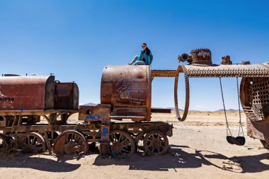 Bir bayan turist eski bir tren vagonunun üstünde oturuyor. Uyuni, Bolivya 'daki tren mezarlığı..
