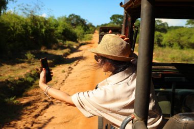 Şapkalı bir kız cipe biner ve selfie çeker. Safari Sri Lanka.