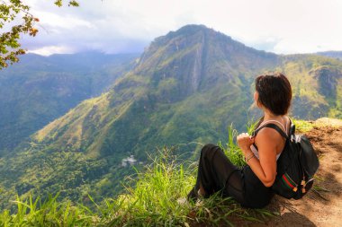 Sırt çantalı bir kadın turist Sri Lanka 'daki Küçük Adam Tepesi' nin tepesinde oturur ve güzel manzaraya hayran kalır..