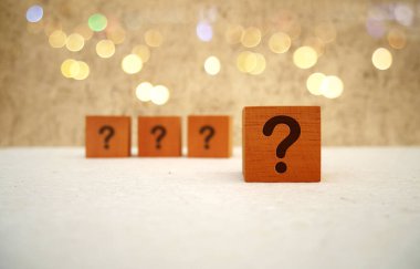 Cube with question mark on white table and bokeh light background. Space for text clipart