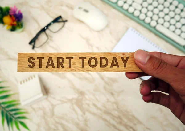 START TODAY - Hand-holding wooden block with Start Today inscription. Keyboard, mouse, notebook, pen, glasses,  and cell phone. To-do list and plans for 2024 Goals for next year.