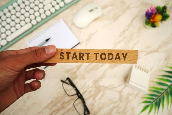 START TODAY - Hand-holding wooden block with Start Today inscription. Keyboard, mouse, notebook, pen, glasses,  and cell phone. To-do list and plans for 2024 Goals for next year.