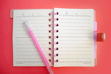 Üst görünüm ya da pembe günlük üzerine düz bir kağıt defter ve pembe arka planda açık pembe bir kalem. Boşluğu kopyala.