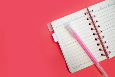Üst görünüm ya da pembe günlük üzerine düz bir kağıt defter ve pembe arka planda açık pembe bir kalem. Boşluğu kopyala.