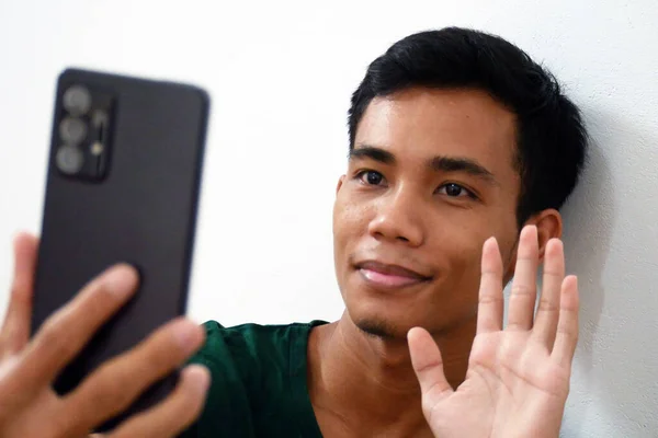 A young Asian man who has migrated far from his family appears to be engaged in a lively conversation via a video call on his smartphone.