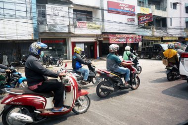 Sürücüler işlek şehir sokaklarında motosiklet sürerler. Güneşli bir günde, şehir caddesinde bir sütun yolcu..