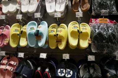 Süpermarketteki müşteriler için çeşitli renk ve boylarda terlikler, sandaletler sergileniyor.
