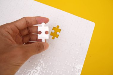 Eller yapboz parçalarını tamamlıyor. İş konsepti. Son görevi tamamla. Sarı arka plandaki bulmacanın beyaz detayları. Beyaz yapboz.