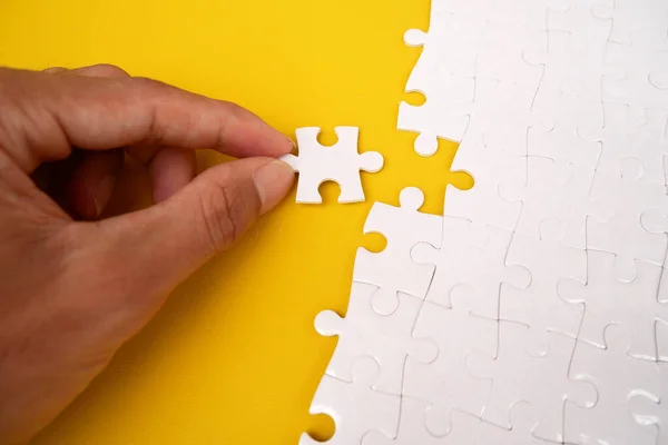 Hands complete missing puzzle pieces. Business concept. Complete the final assignment. White details of the puzzle on a yellow background. White jigsaw puzzle.
