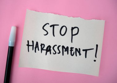 Mesajlı beyaz kağıt, pembe arka planda siyah kalemle yazılan tacizi durdurur.