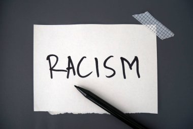 Gri arka planda ırkçılık metni olan beyaz bir kağıt. Kağıt, kalem ve ırkçılık metniyle teselli edici. Irkçılık konsepti. Ayrımcılık, ırk sorunları