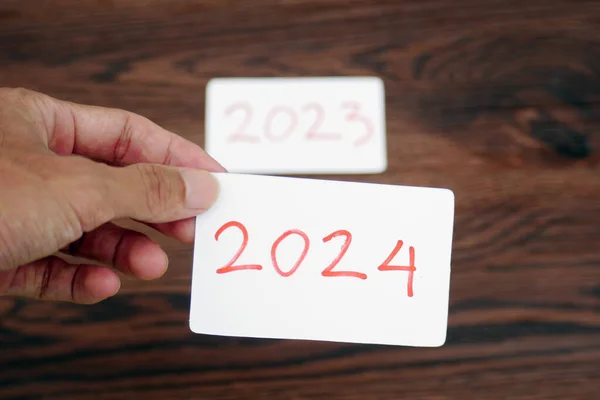 The hand takes the 2024 card leaving the 2023 card behind it. Beginning of new year 2024. New year preparation, life, business, plans, goals, targets and strategy concept.