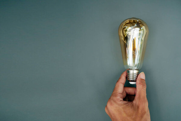 Hand holding yellow light bulb on gray background. Economical energy saving light bulb concept in man's hand. copy space