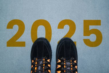 2025 yılbaşı konsepti. 2025 metni asfalt yolda yazılmış ve erkek koşucu yeni yılı karşılamaya hazırlanıyor. Başarı, kariyer, zorluklar ve değişimin başlangıcına doğru kavram.