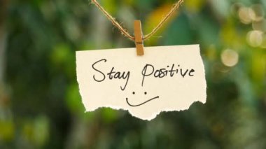 Olumlu düşün - Yırtık kağıt, metin, pozitif kal, ipte sallan, doğa, arka planda batıyor.