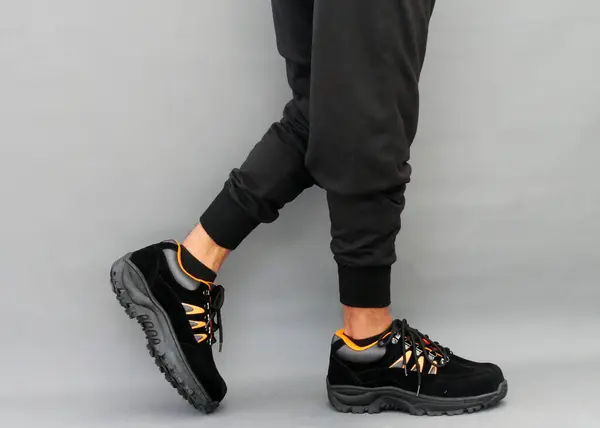 stock image A male model wears black suede shoes with orange accents, featuring a sturdy, meshed sole, standing out against the plain gray background, showing its rugged durability and stylish design