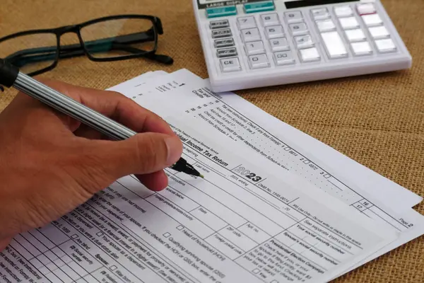 stock image Businessman's hand is writing on a tax form, there is a calculator and glasses on the table