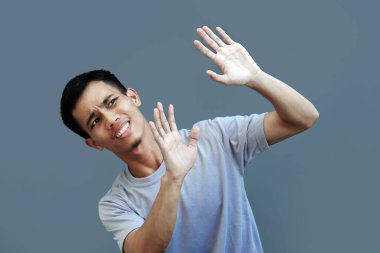 Endişeli ve korkmuş bir ifadeye sahip genç bir adam, kolları bir saldırıya karşı savunma pozisyonunda, gözleri korkuyla dolu..