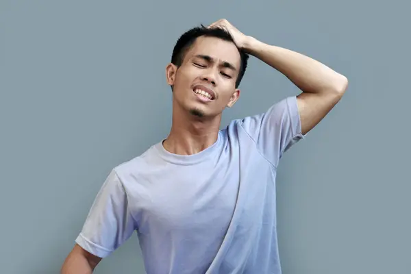 stock image A young Indonesian man is seen holding his hair with one hand and expressing pain, as if his hair was being pulled