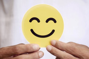 Sarılar içinde gülümseyen bir yüzü tutan eller. Pozitif müşteri memnuniyeti değerlendirmeleri, akıl sağlığı, iltifatlar, dünya ruh sağlığı günü