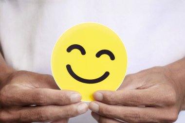 Sarılar içinde gülümseyen bir yüzü tutan eller. Pozitif müşteri memnuniyeti değerlendirmeleri, akıl sağlığı, iltifatlar, dünya ruh sağlığı günü