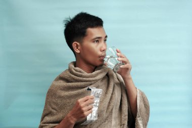 Genç Endonezyalı bir adam bir bardak suyla hap alıyor. Kişisel bakım ya da hastalık tedavisi kavramı.