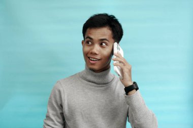 Genç Asyalı bir adam hoş ve şaşırtıcı bir ifadeyle arıyor. Arkaplan açık mavi.