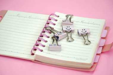 Gülümse emoji ataç kağıdı pembe arkaplanlı spiral defter üzerine