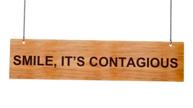 Üzerinde kırmızı metin olan tahta bir tahta. Gülümseme mutlu bir yüzdür. Beyaz bir duvarda asılı.