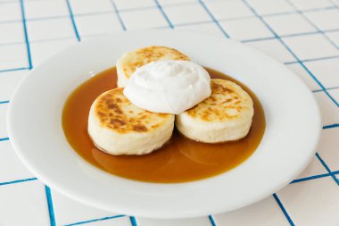 Zarif, beyaz bir tabak. Üstünde bol miktarda kremayla süslenmiş üç tane lezzetli krep var.