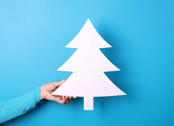 white christmas tree in hand over blue background, happy new year concept